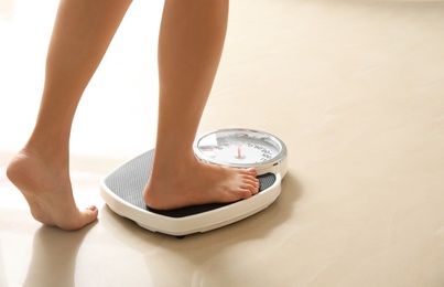 Woman stepping on floor scales indoors, space for text. Overweight problem