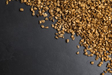 Pile of gold nuggets on black table, flat lay. Space for text
