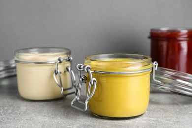 Jars with mustard, mayonnaise and ketchup on light grey table, closeup