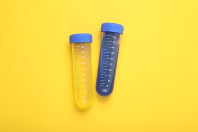 Photo of Test tubes with colorful liquids on yellow background, flat lay. Kids chemical experiment set
