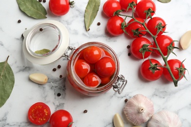 Glass jar of pickled cherry tomatoes on white marble table, flat lay