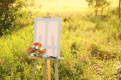 Wooden easel with blank canvas and painting equipment in meadow. Space for text