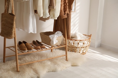 Rack with stylish shoes and women's clothes in dressing room. Modern interior design