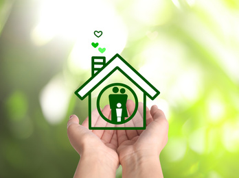 Woman demonstrating illustration of house with family on blurred green background, closeup