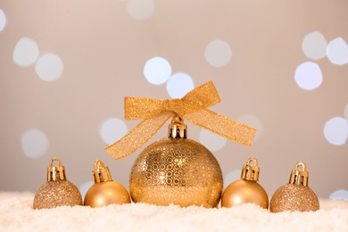 Beautiful golden Christmas balls on snow against blurred festive lights