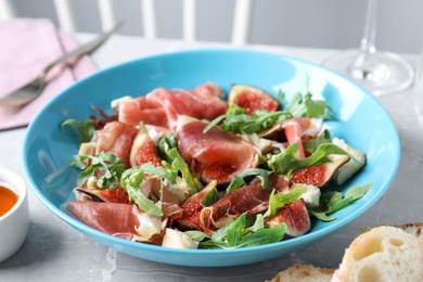 Salad with ripe figs and prosciutto served on grey marble table indoors, closeup