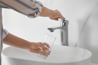 Woman filling glass with water from faucet over sink, closeup