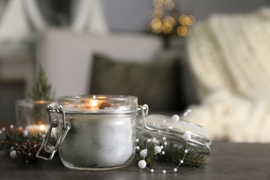 Burning scented conifer candle and Christmas decor on grey table indoors. Space for text