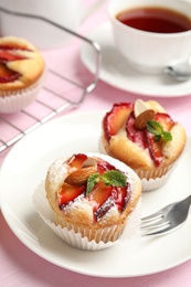 Delicious cupcakes with plums on pink wooden table