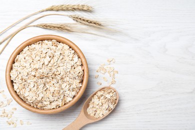 Photo of Oatmeal, bowl, spoon and spikelets on white wooden table, flat lay. Space for text