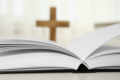 Open Bible on table and blurred cross on background, closeup. Christian religion