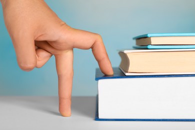 Woman imitating stepping up on books with her fingers against light blue background, closeup