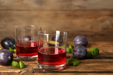 Delicious plum liquor, mint and ripe fruits on wooden table. Homemade strong alcoholic beverage
