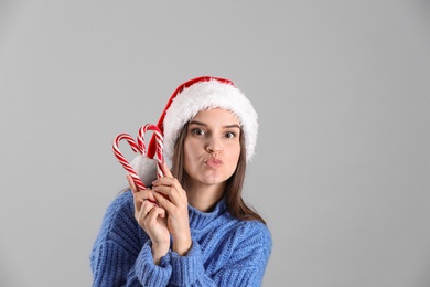 Pretty woman in Santa hat and sweater making heart with candy canes on grey background