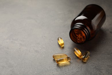 Overturned bottle with dietary supplement capsules on grey table. Space for text