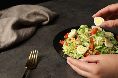 Woman making delicious salad with Chinese cabbage and quail eggs at black table, closeup
