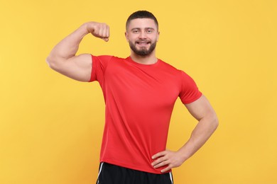 Photo of Portrait of handsome man showing muscles on yellow background