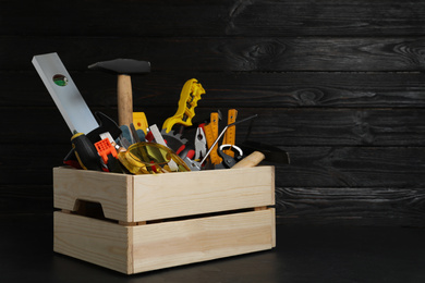 Wooden crate with different carpenter's tools on black table. Space for text