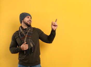 Happy young man in warm clothes on yellow background, space for text. Winter vacation