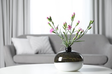 Vase with beautiful carnation flowers on table in living room, space for text. Stylish element of interior design