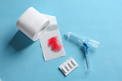 Anoscope, suppositories and toilet paper with red feather on light blue background, flat lay. Hemorrhoid treatment