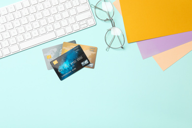 Credit cards, computer keyboard and glasses on light blue background, flat lay. Space for text