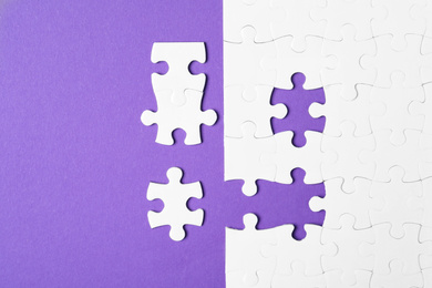 Blank white puzzle with separated pieces on purple background, flat lay
