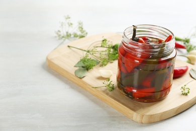 Glass jar of pickled chili peppers and ingredients on white table. Space for text