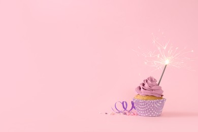 Birthday cupcake with burning sparkler, streamer and sprinkles on pink background. Space for text