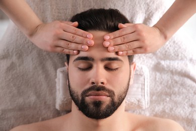 Young man receiving facial massage in beauty salon, top view