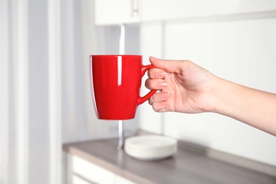 Woman holding red cup at home, closeup