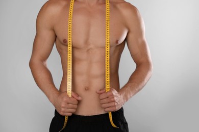 Shirtless man with slim body and measuring tape on grey background, closeup