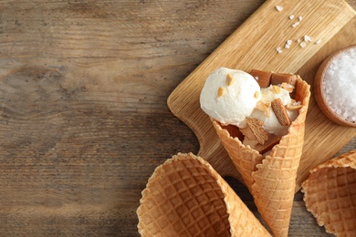Waffle cone with ice cream, caramel and nuts on wooden table, top view. Space for text