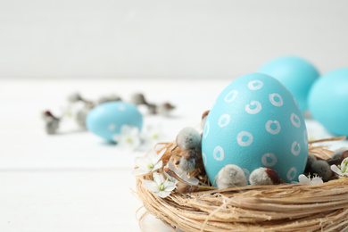 Colorful Easter egg in decorative nest on white table, closeup. Space for text