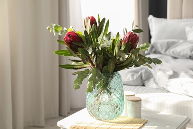 Photo of Vase with bouquet of beautiful Protea flowers on white table in bedroom