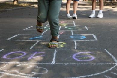 Little African American girl playing hopscotch drawn with chalk on asphalt outdoors, closeup. Happy childhood