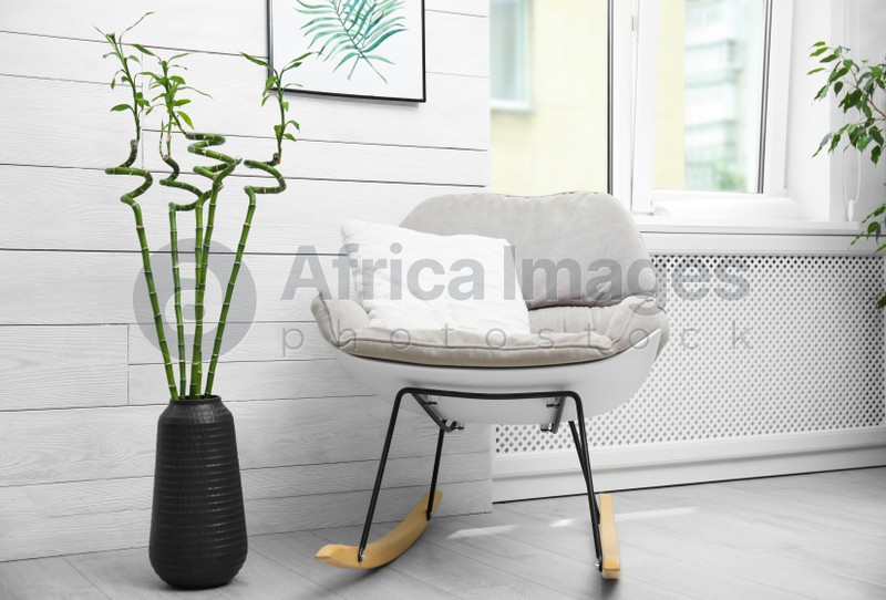Vase with green bamboo stems and stylish rocking chair in room. Interior design