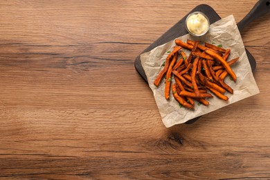 Board with delicious sweet potato fries and sauce on wooden table, top view. Space for text