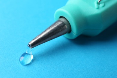 Photo of Melted glue dripping out of hot gun nozzle on light blue background, closeup