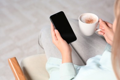 Photo of Woman with smartphone and cup of coffee indoors, closeup. Space for text