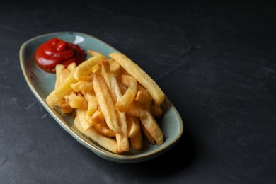 Photo of Plate of tasty french fries served with ketchup on black table