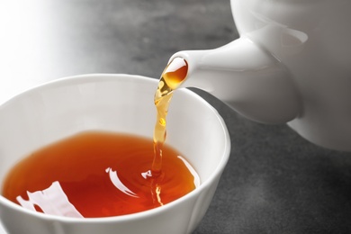 Pouring black tea into white porcelain cup on gray table, closeup