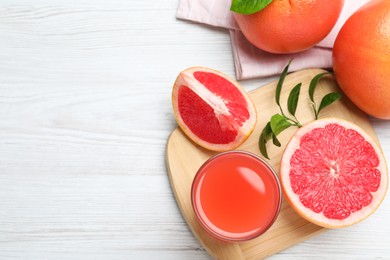 Tasty freshly made grapefruit juice and fruits on white wooden table, flat lay. Space for text