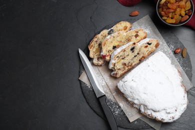 Traditional Christmas Stollen with icing sugar on black table, flat lay. Space for text