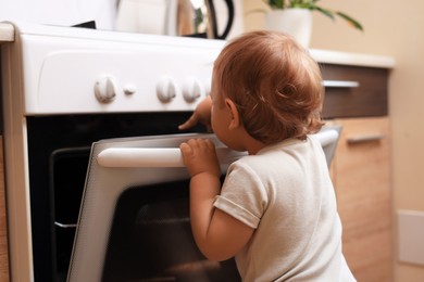 Little child opening oven indoors. Dangers in kitchen