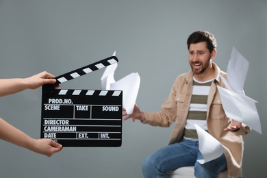Photo of Emotional actor performing while second assistant camera holding clapperboard on grey background, closeup