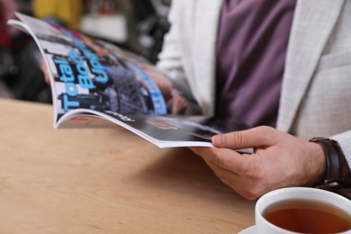 Young man reading sports magazine at table indoors, closeup