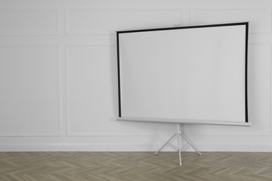 Blank projection screen near white wall indoors. Space for design