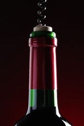 Opening wine bottle with corkscrew on dark red background, closeup