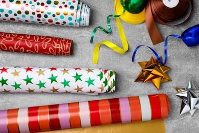 Different colorful wrapping paper rolls, gift bows and ribbons on grey table, flat lay